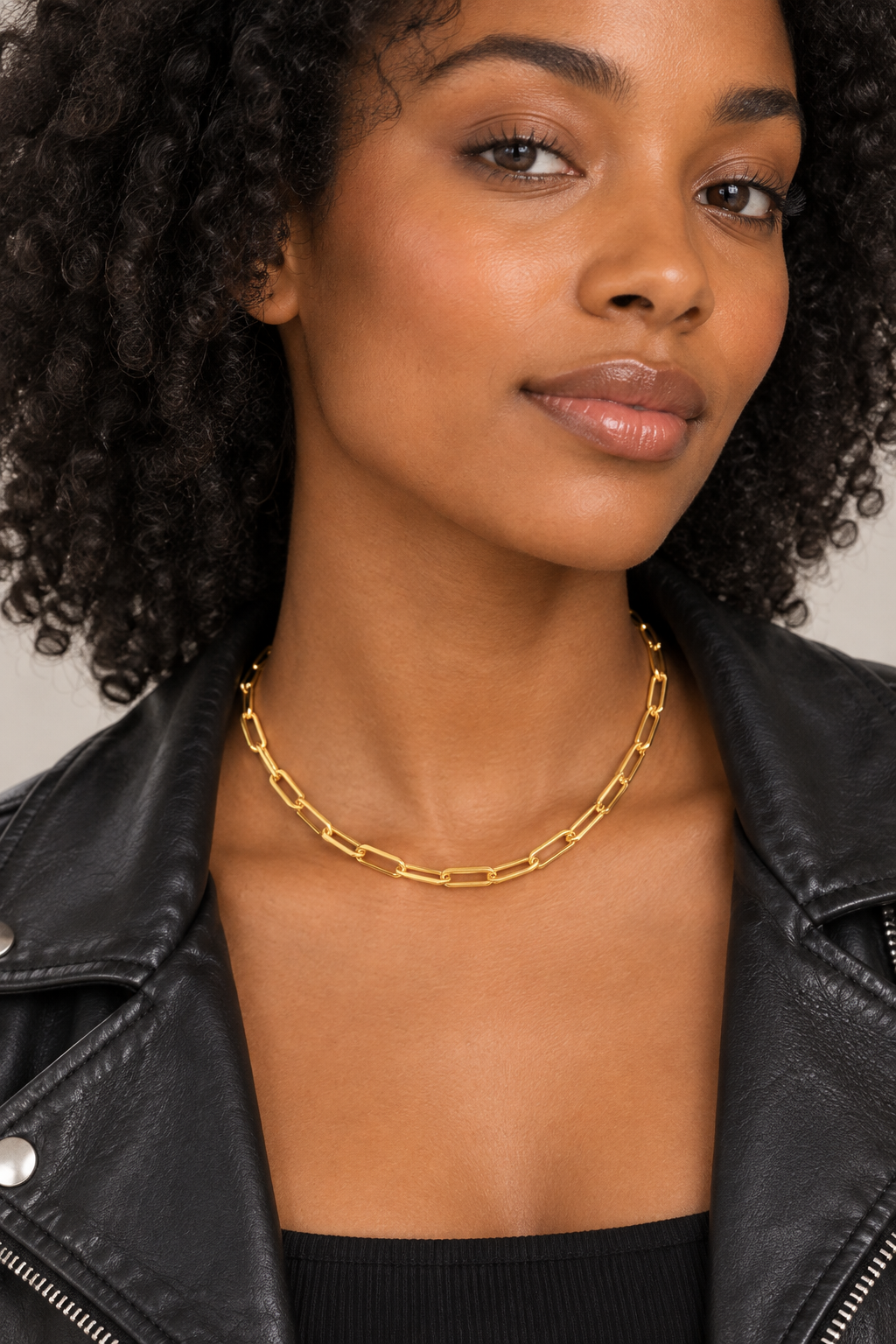 Black model with curly hair in a black leather jacket wearing the gold paper clip chain necklace